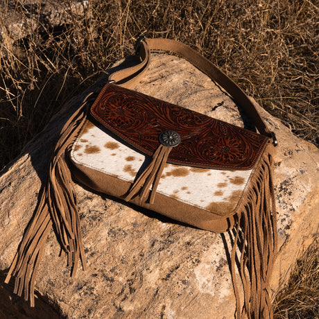 Brown leather handbag with fringe on a stone surface