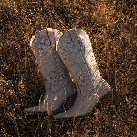Pair of white cowboy boots in a field of dry grass