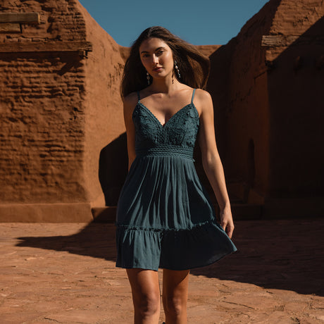 Woman in a teal dress standing in front of a red brick wall.